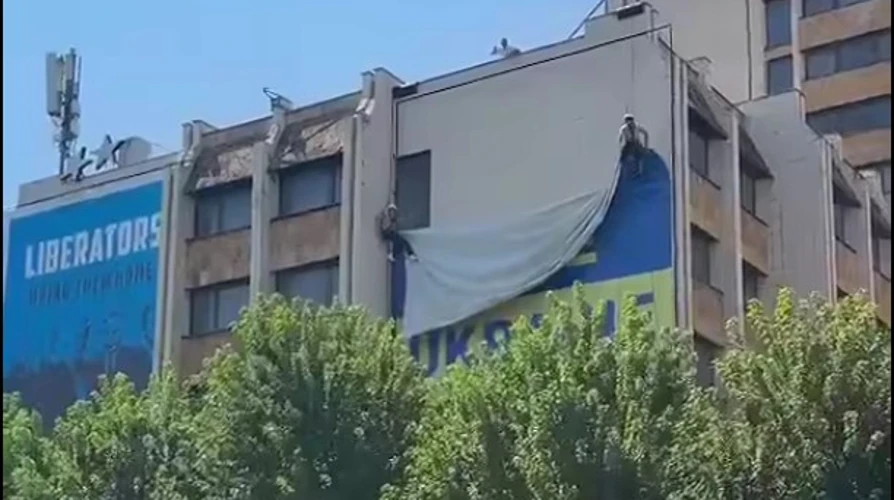 Великий синьо-жовтий український прапор на будівлі у центрі Приштини та момент його зняття